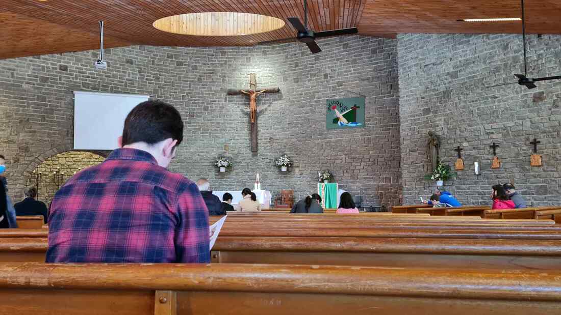 A young man sitting in a church, separate from everyone else there.